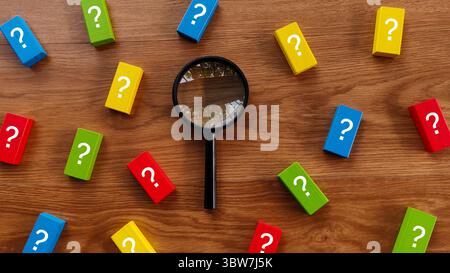Finding Answers: Magnifying Glass Amidst Question Blocks Stock Photo