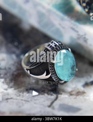 Silver men's ring with a large blue gemstone and black stones lying on a stone surface is sparkling Stock Photo