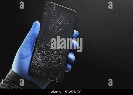 A broken touch phone with a cracked screen in your hand on a black background. Close-up Stock Photo