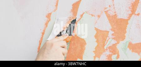 Young man using spatula and plastering of wall with white fresh finishing putty. Closeup. Repair work of home. Empty place for text. Side view Stock Photo