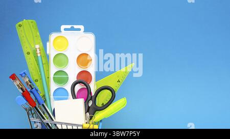 School stationery in a toy shopping cart on a blue background. The concept of preparing for the beginning of the school year. Copy space Stock Photo