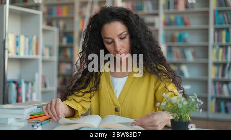 Indian Hispanic woman girl student teacher reading book textbook yawning tired library high school university college exam overworked sleepy learning Stock Photo