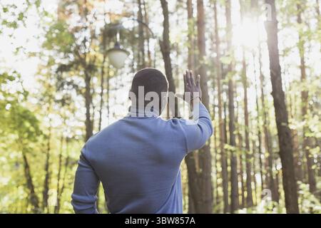 African american man breathing fresh and looking on sun standing in spring park outdoors. Well being and relaxation concept Stock Photo