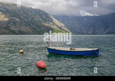 Storm brewing over Kotor Bay, with empty fishing boat tethered in the foreground in autumn. Kotor Bay is known for its dramatic weather patterns throu Stock Photo
