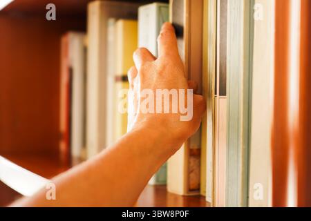 Close-up of a woman's hand trying to retrieve a book from a bookshelf,  Concepts of reading, knowledge, and information Stock Photo