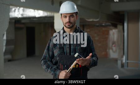 Confident man Caucasian guy builder in hard hat engineer holding hammer on construction site building renovation Caucasian male repairman architect Stock Photo