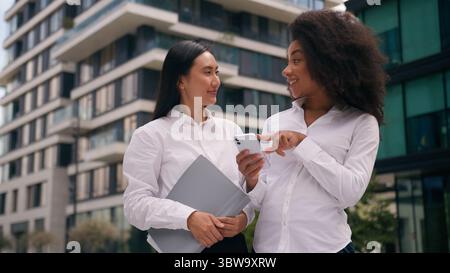 African American Asian Korean women females colleagues businesswomen business using mobile phone smartphone online discuss talking social media Stock Photo