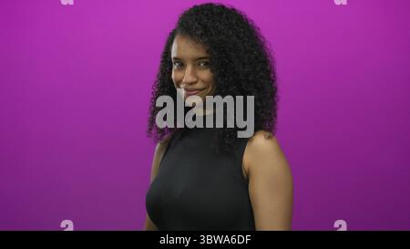 Young smiling friendly woman standing confidently beckons with finger against pink studio wall; invitation. Stock Photo