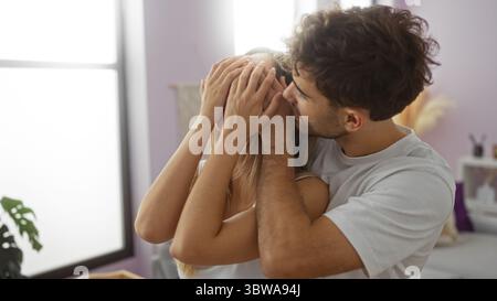 Man playfully covers woman’s eyes in a loving couple moment indoors, under soft natural light, creating an intimate and joyful atmosphere in the cozy Stock Photo