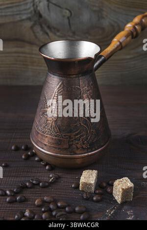 Ancient coffee maker, scattered coffee beans and pieces of sugar cane are on a dark wooden background, vertical image Stock Photo