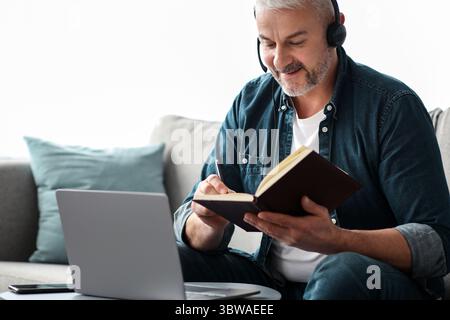 Happy old man having online class, using laptop and headset Stock Photo