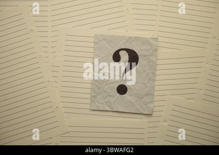 Crumpled gray paper note with question mark on it lying on lined notebook pages. Stock Photo