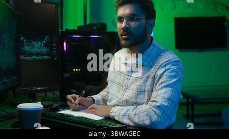 Indian Arabian man businessman programmer hacker IT specialist business male ethnic guy studio home coder trader writing notes code information data Stock Photo