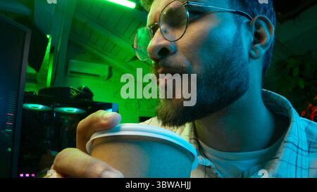 Pensive Caucasian man professional software engineer guy male coder programmer crypto specialist drinking coffee workplace looking computer thinking Stock Photo