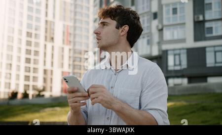 Pensive Caucasian man using mobile phone smartphone thinking thoughtful guy ponder looking around gps navigator maps online male businessman city Stock Photo