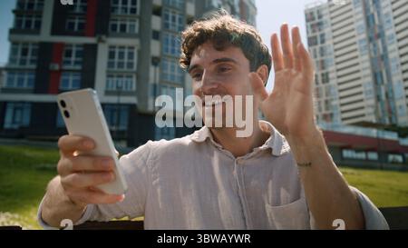 Caucasian man using mobile phone smartphone online meeting greeting waving headphones city male guy businessman blogger communication talking video Stock Photo
