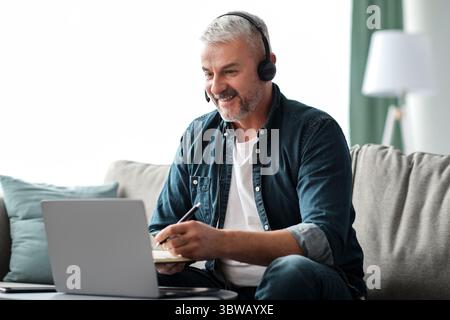 Excited mature man studying online, using laptop and headset Stock Photo