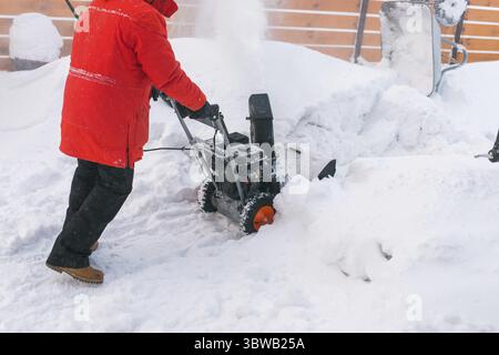 Closeup of red snow blower in action. Senior mature man outdoor in front of house using snowblower machine for removing snow on yard. Snow thrower in Stock Photo