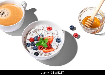 Healthy breakfast with chia bowl and cappuccino coffee isolated on white background, trendy design with hard light. Chia pudding with berries and hone Stock Photo