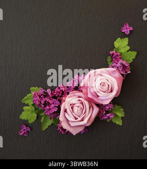 Decorative composition consisting of pink roses, violet lilac flowers and green leaves on a black slate. Flat lay, top view, overhead view Stock Photo