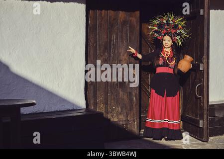 Beautiful brunette lady with a long dark hair, in a black and red ukrainian embroidered authentic national costume, beads and a wreath of colorful flo Stock Photo