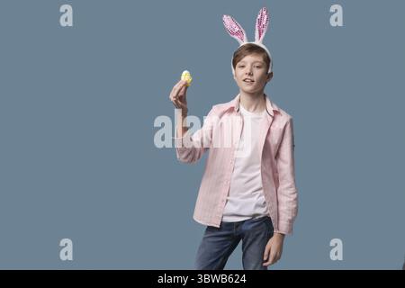 Guy with bunny ears with colourful Easter eggs in his hand in pink shirt. Gesticulating with different funny facial expressions. A boy in a rabbit cos Stock Photo