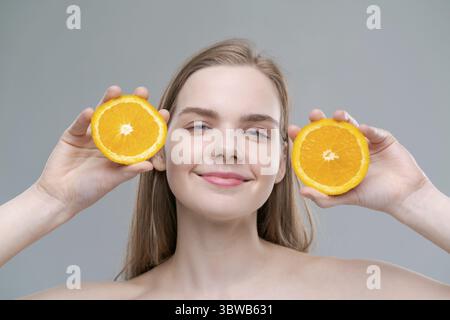 A woman is holding two oranges in her hands and smiling. Concept of happiness and positivity, as the woman is enjoying the moment. The oranges symboli Stock Photo