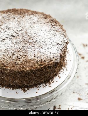 Chocolate cake with chocolate shavings and powdered sugar is sitting on a glass cake stand Stock Photo