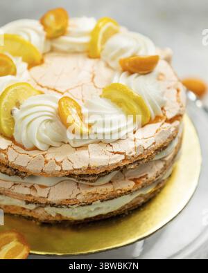 Layered meringue cake topped with lemon and kumquat slices and whipped cream swirls is waiting to be eaten Stock Photo