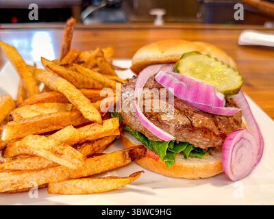 Close up view of a succulent burger with hand cut fries, onion and gherkin on a fresh bun Stock Photo