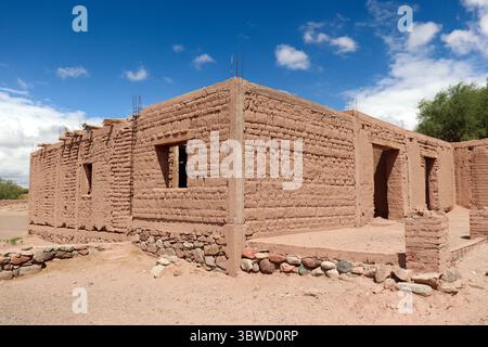 Partially built or ruined adobe structure, showing raw earth bricks. Located near the Mayorazgo Church in Catamarca, Argentina, under a blue sky. Stock Photo