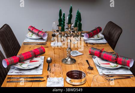 Festive wooden table setting with red Christmas crackers, green candles, silverware, and plates prepared for a holiday meal Stock Photo