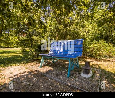 Big blue bench in woodland oasis of relaxation in Fossano, Piedmont, Italy Stock Photo