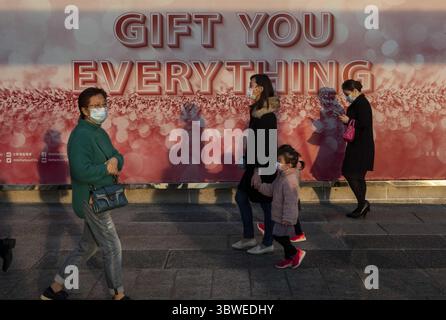 December 19, 2020, Hong Kong, China: Pedestrians wearing face masks walk past a large size Christmas theme banner at the entrance of a shopping mall in Hong Kong..Hong Kong is currently experiencing a four wave of COVID-19 cases while the government has implemented new social restrictions and rules in the city. (Credit Image: © Miguel Candela/SOPA Images via ZUMA Wire) Stock Photo