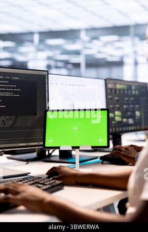 System administrator in server hub ensuring data remains shielded from potential threats using mockup tablet. African american worker safeguarding data center against hackers with green screen device Stock Photo