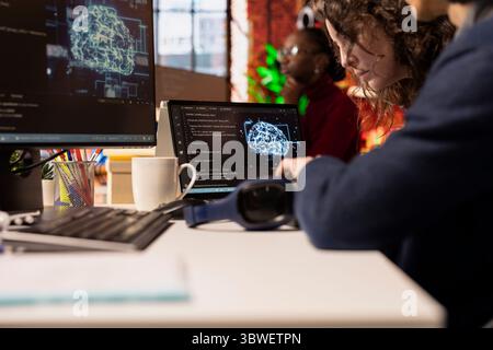 IT engineers cooperating in AI focused startup overseeing worker designing, coding and debugging applications. Close up of coworkers brainstorming, doing code testing and quality assurance Stock Photo