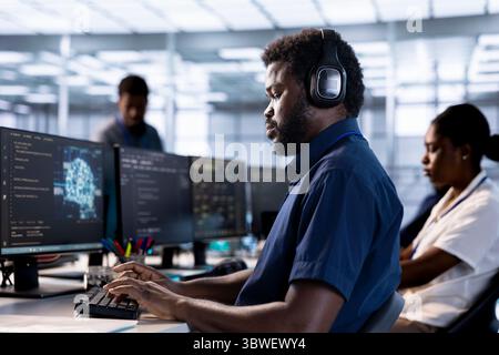 Server farm IT specialist listening music while doing AI research, implementing algorithms using neural networks. Developer in data center wearing headphones, using artificial intelligence Stock Photo