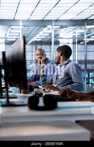 Team of engineers chitchatting in data center while running system diagnostic tests and error checking utilities. Coworkers looking for network issues affecting server performance and connectivity Stock Photo