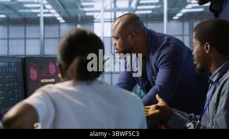 Cybersecurity specialists in server room trying to protect equipment from hacker stealing data. Programmers in data center office doing teamwork to delete virus attacking company servers, camera A Stock Photo