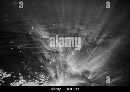 A black and white photo of water with a lot of bubbles. The bubbles are scattered throughout the water, creating a sense of movement and energy. The p Stock Photo
