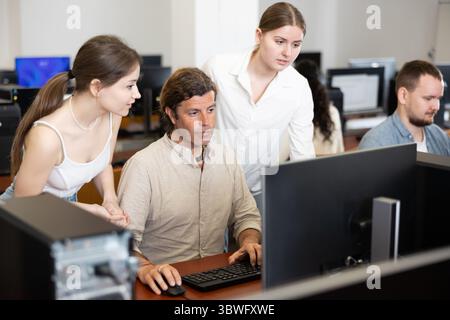 Two female friend companions stands next to computer courses male student Stock Photo