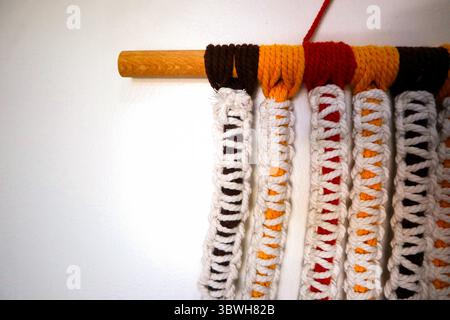 Colorful tassel wall hanging with braided white yarn and vibrant threads in yellow, red, and brown on white background Stock Photo