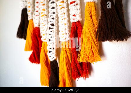 Colorful tassel wall hanging with braided white yarn and vibrant threads in yellow, red, and brown on white background Stock Photo