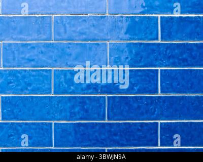 A close-up of a wall featuring various shades of blue rectangular tiles, creating a textured and gradient effect across the surface. Stock Photo