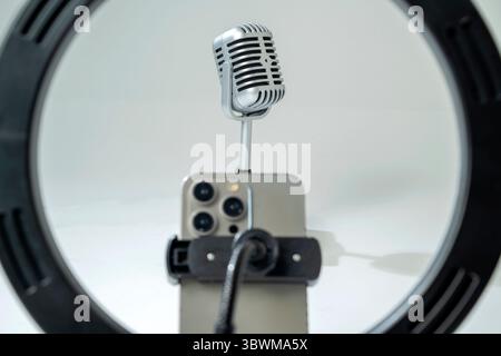 Round LED ring light with a cellphone on a phone holder with a vintage silver microphone with a white background. Vlogging or live streaming equipment Stock Photo