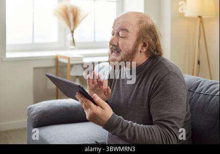 Senior mature man looking at tablet having video call sitting on sofa in living room at home Stock Photo