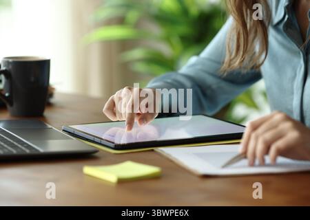 Close up portrait of an office worker scrolling on tablet checking statistics on document on wooden table Stock Photo