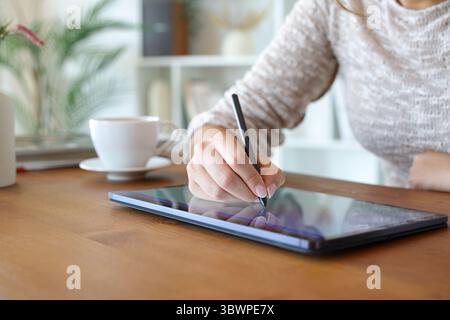Close up of a woman hands drawing or handwriting with digital pen on tablet at home Stock Photo