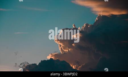 Close-up view of dramatic cumulonimbus clouds illuminated by sunlight at sunset, set against a clear sky. Stock Photo