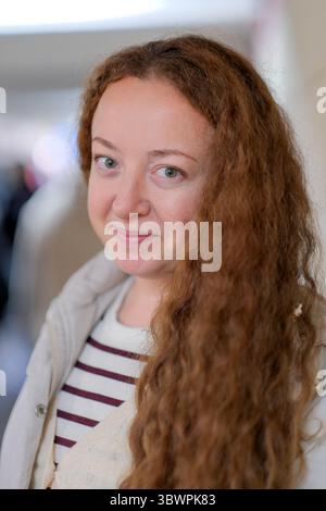 A cheerful woman with long curly hair smiles warmly while indoors, embracing joy. Stock Photo